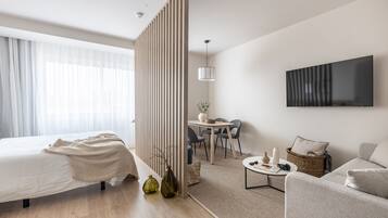 Una habitación de hotel moderna con una cama, un escritorio, una silla, un sofá, un televisor y una planta decorativa.