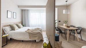 A modern hotel room with a large bed, bedside tables, a dining area with chairs, and a view of the outdoors. - Líbere Madrid Chamberí (Madrid)
