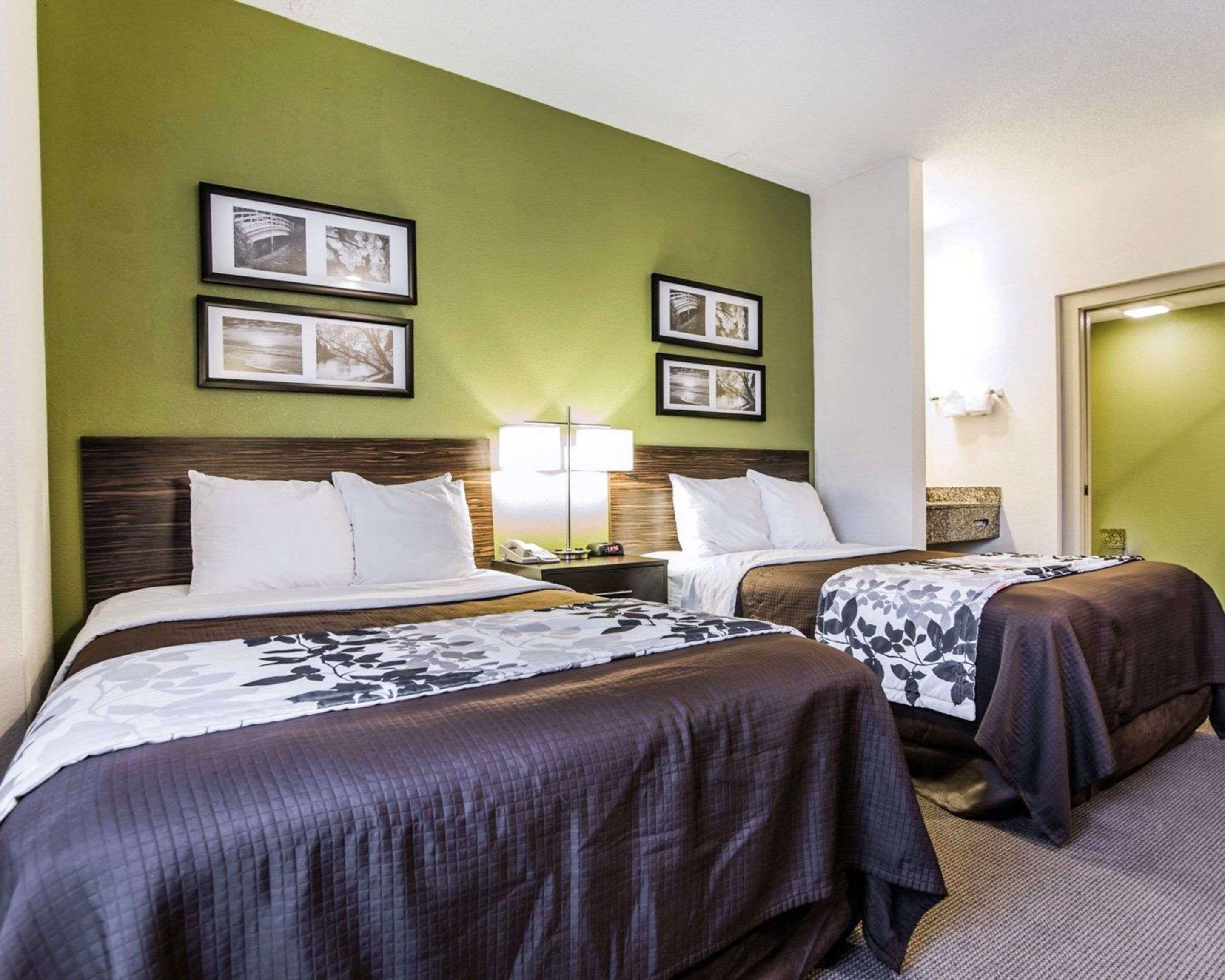 A hotel room with two beds, green walls, framed pictures, and a nightstand with a lamp.