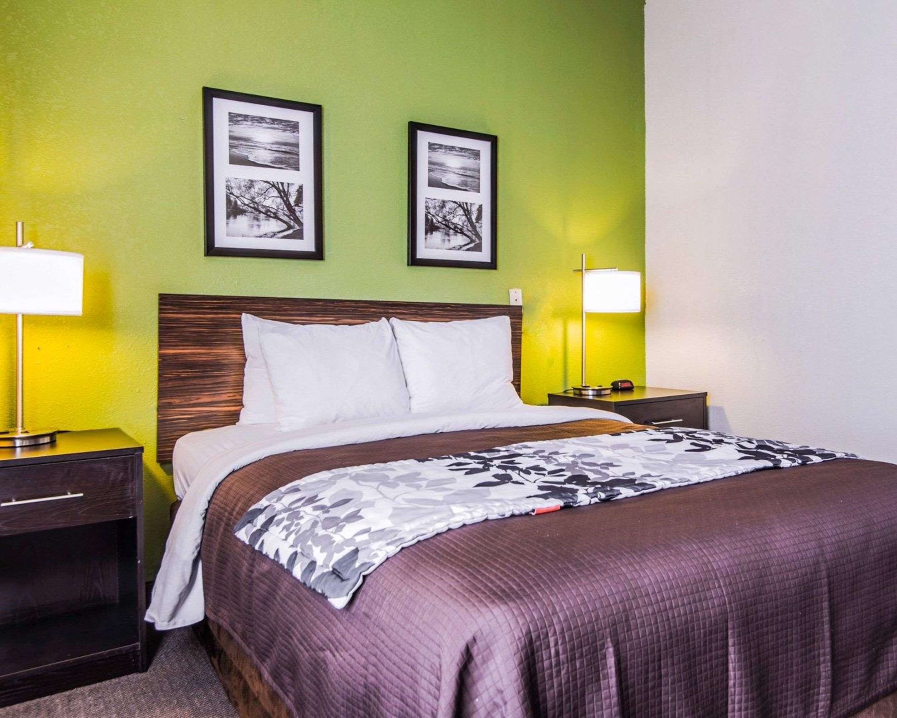 Une chambre d’hôtel comprenant un lit, deux tables de chevet, une petite table, une lampe et deux tableaux encadrés accrochés au mur.