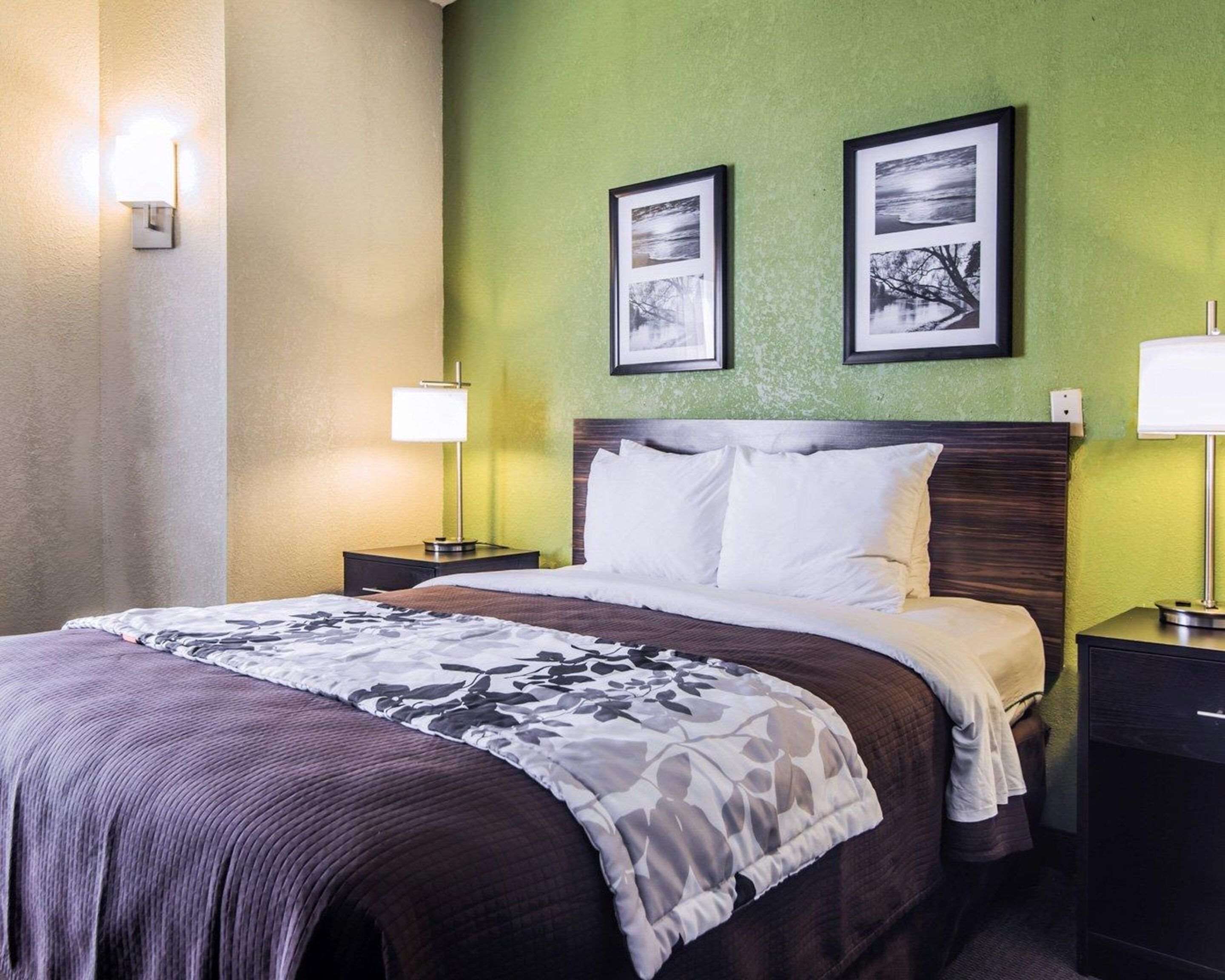 A hotel room with a bed, two bedside lamps, and two framed pictures on the wall.