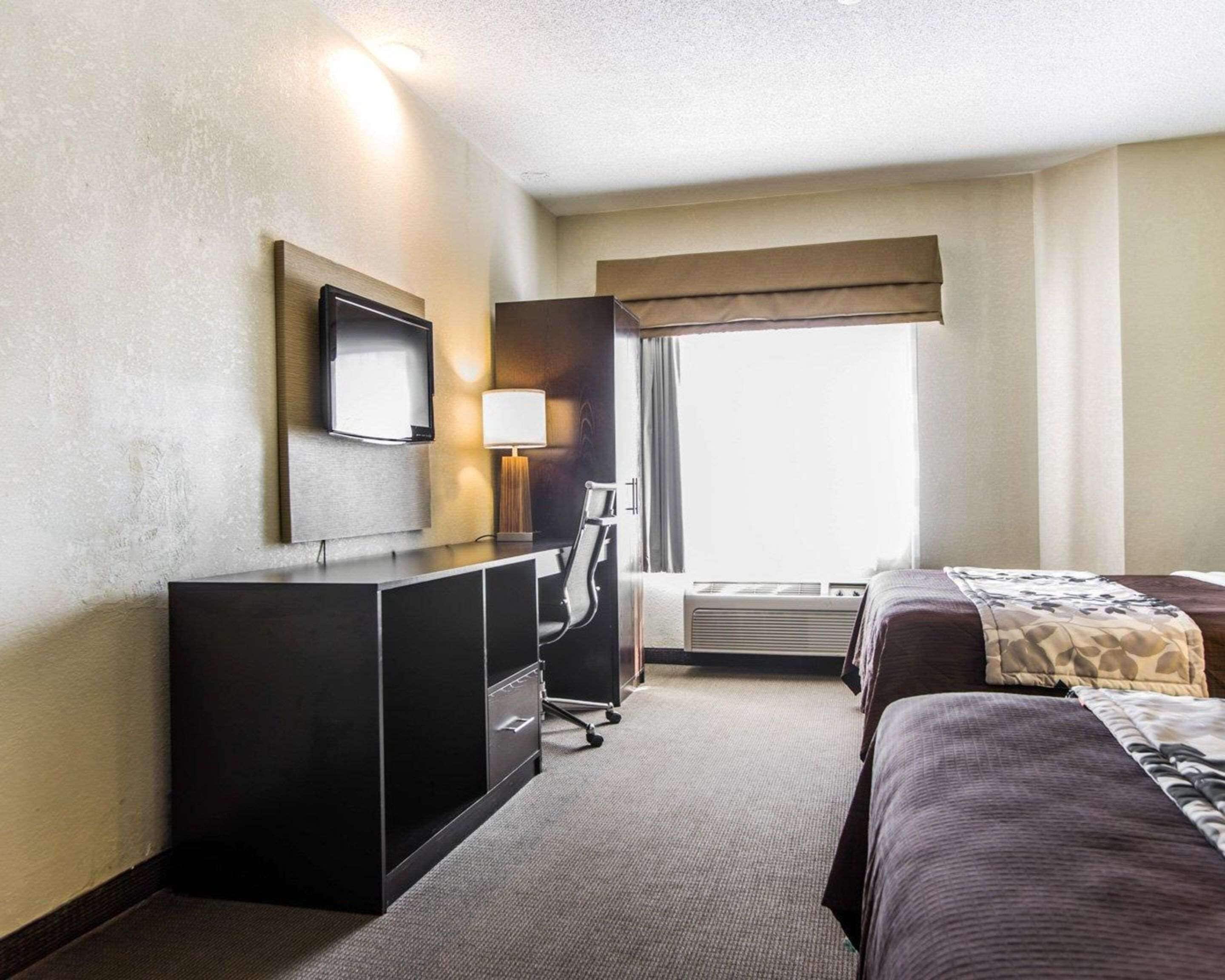 Ein Hotelzimmer mit Bett, Schreibtisch mit Stuhl, Fernseher und einem Fenster mit Vorhängen.