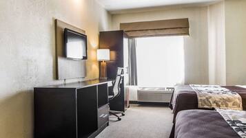 Ein Hotelzimmer mit Bett, Schreibtisch mit Stuhl, Fernseher und einem Fenster mit Vorhängen.