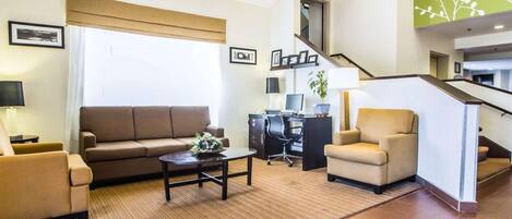 A modern living room with a sofa, armchair, and coffee table, a desk with a computer, and a staircase leading to an upper level.