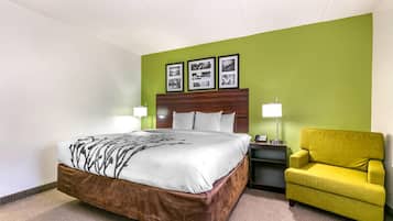 Une chambre d’hôtel avec un grand lit, un fauteuil jaune, une table de chevet avec une lampe et trois tableaux encadrés accrochés au mur.