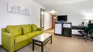 Hotellihuoneessa on vihreä sohva, pieni pöytä, työpöytä, jossa on tietokone ja televisio, sekä mikroaaltouuni.