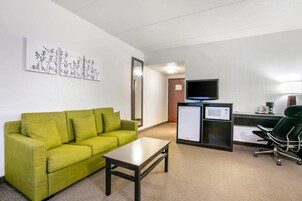 Habitación de hotel con un sofá verde, una mesita, un escritorio con computadora y televisión, y un microondas.