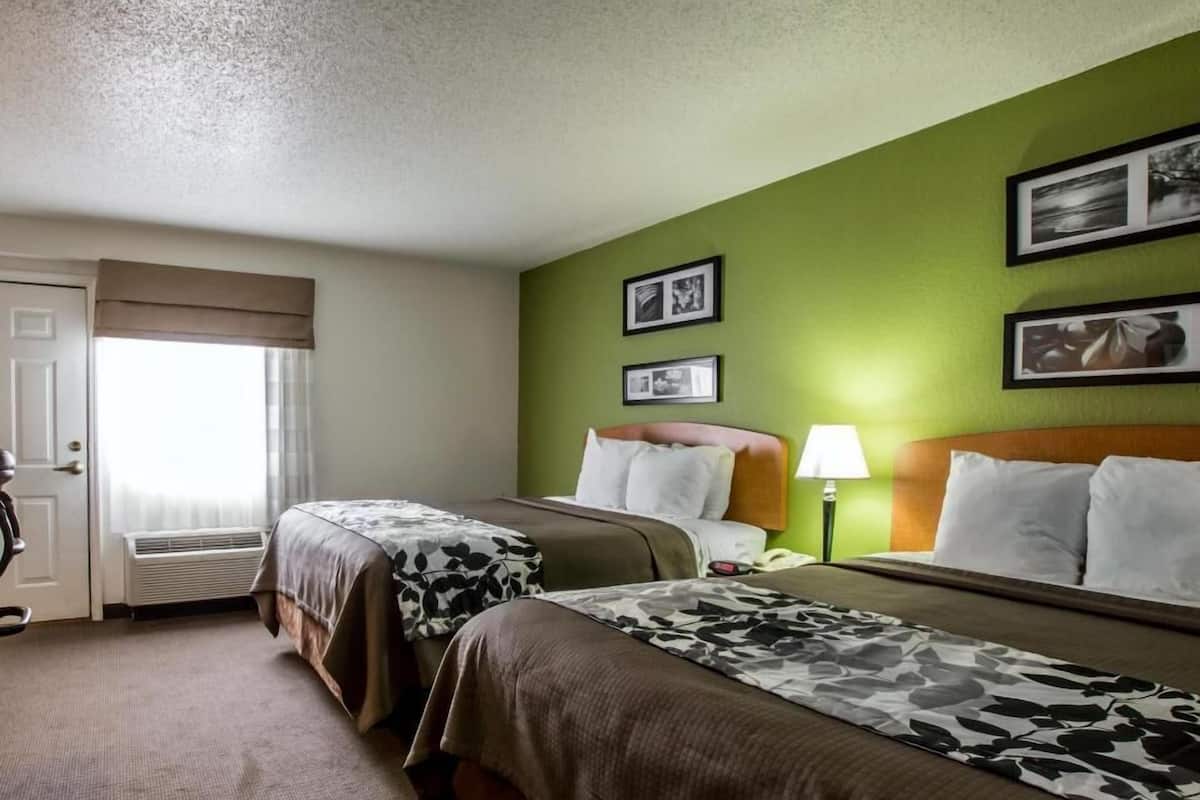 Une chambre d’hôtel avec deux lits, une fenêtre avec des rideaux, une porte et un mur orné de tableaux.