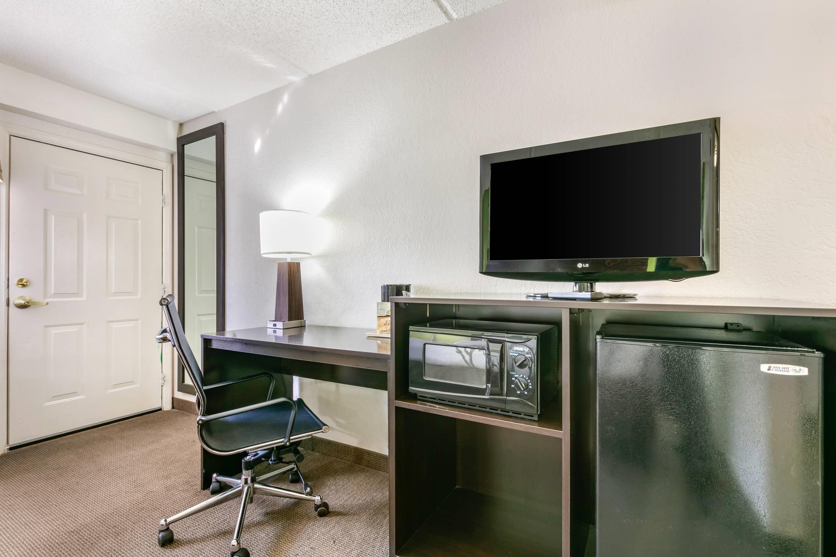 A hotel room with a desk, a television, a microwave, and a refrigerator.