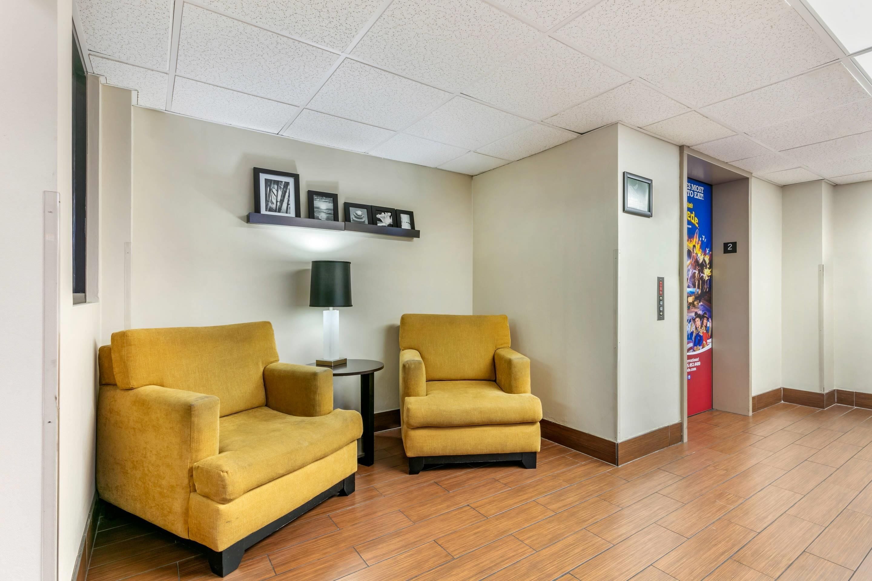 A lobby with two yellow armchairs, a small table, framed pictures on the wall, and a red door with a poster.