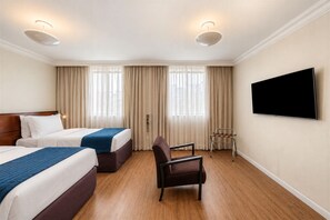 Ett hotellrum med två sängar, en TV, en stol och ett fönster med gardiner.