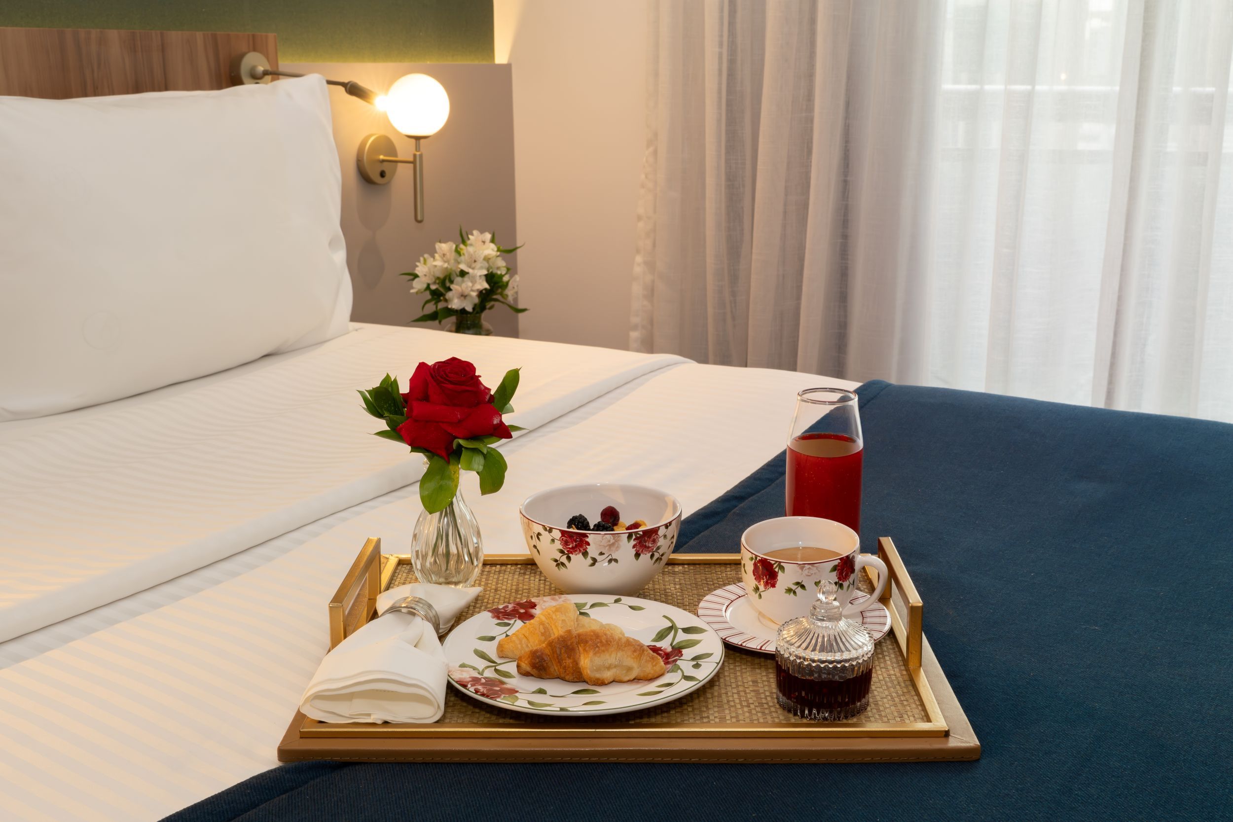 A neatly made breakfast tray with croissants, a bowl of fruit, a cup of coffee, and a glass of juice on a bed.