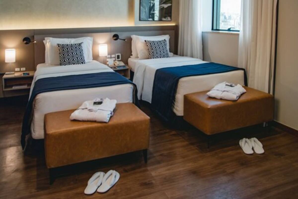 A hotel room with two beds, a wooden floor, and a window with curtains.