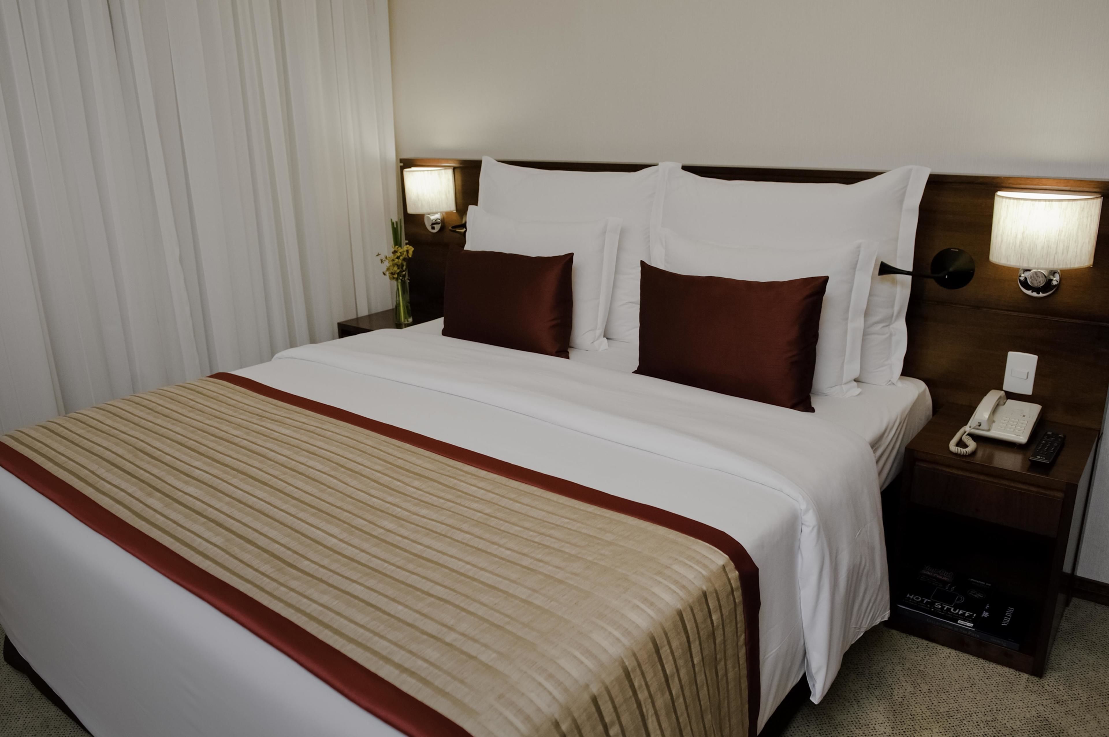 Una habitación de hotel con una cama grande, dos mesitas de noche con lámparas, un teléfono y una mesita con lámpara.