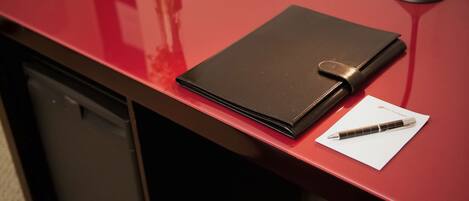 A desk with a black notebook, a pen, a lamp, and a vase with flowers.