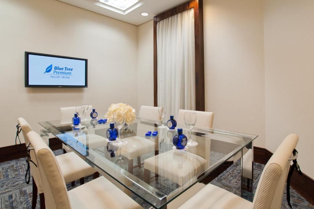 Un salón de conferencias con una mesa de vidrio, sillas blancas y un letrero Blue Tree Premium en la pared.