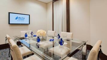 Un salón de conferencias con una mesa de vidrio, sillas blancas y un letrero Blue Tree Premium en la pared.