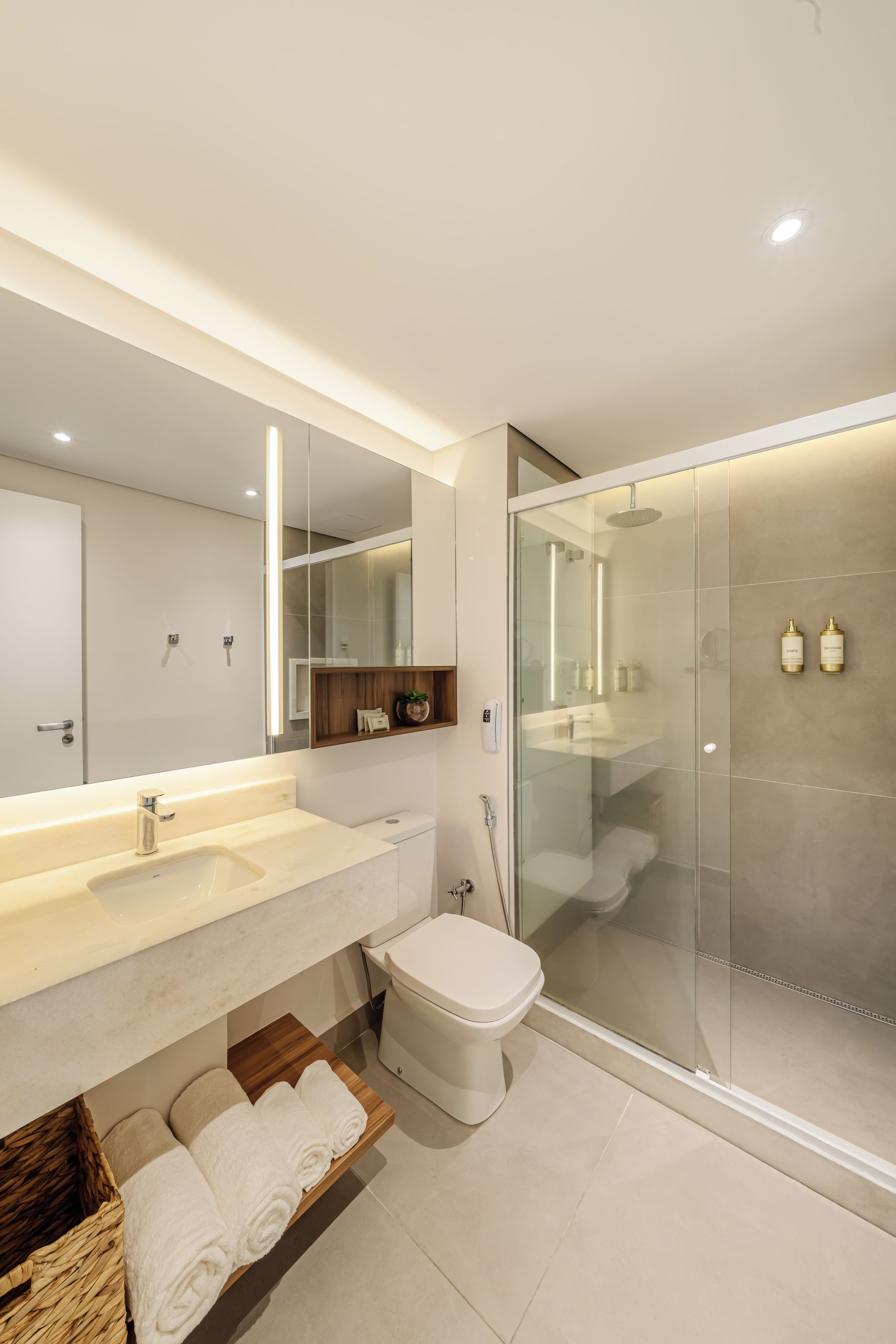 A modern bathroom with a large mirror, dual sinks, a toilet, and a glass-enclosed shower.