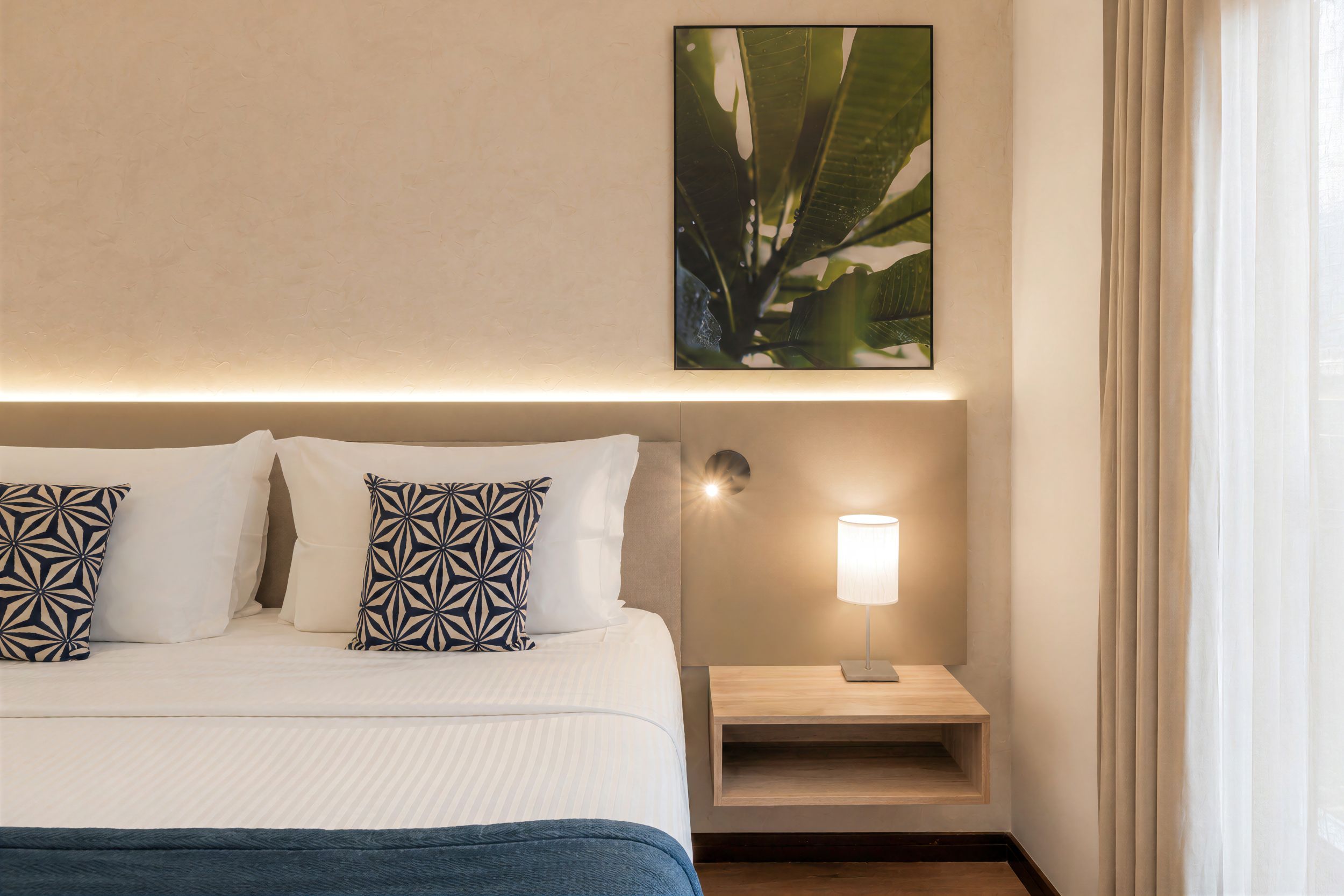 Habitación de hotel con cama, almohadas, mesita de noche, lámpara y un cuadro colgado en la pared.