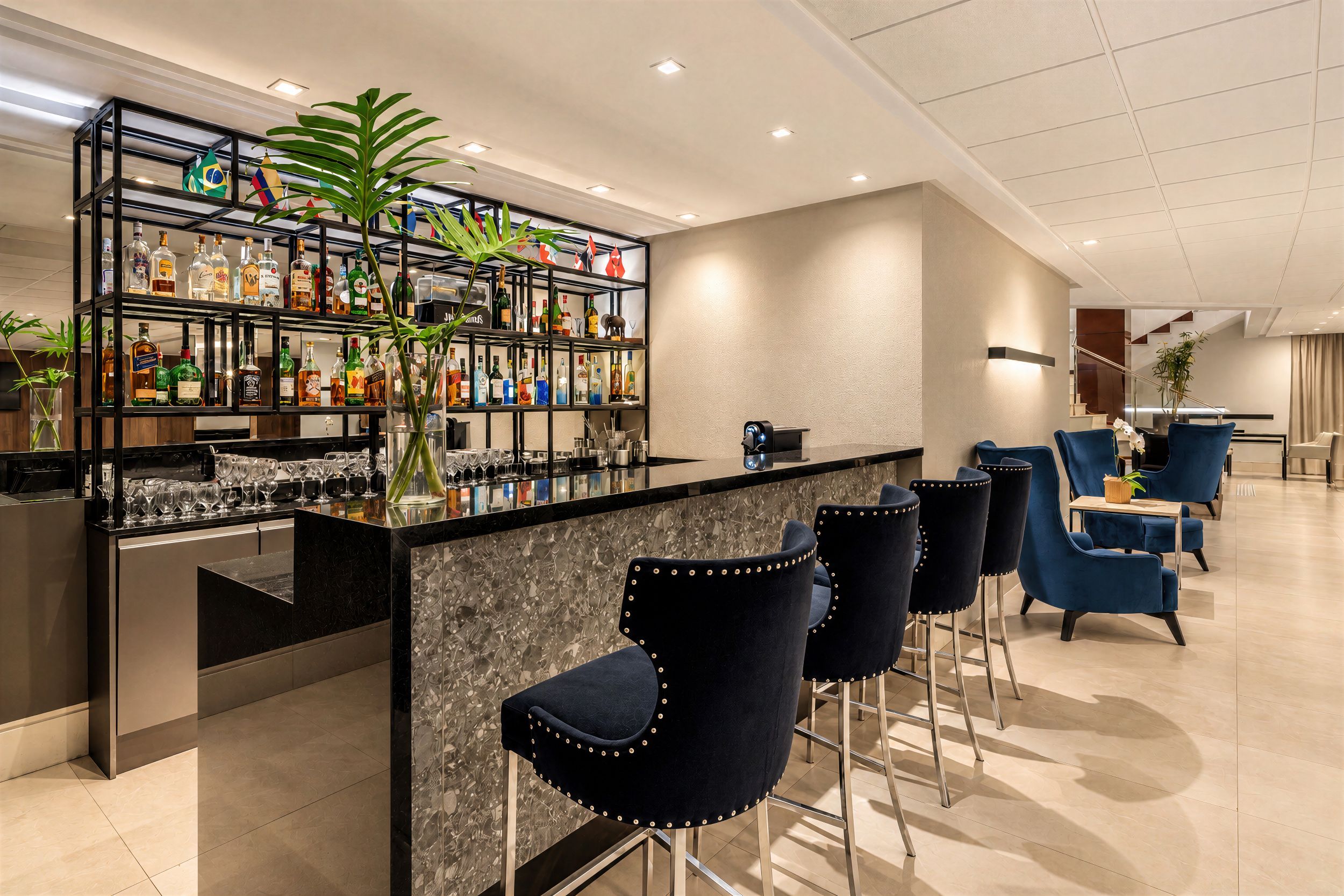 Eine Bar mit einer Marmorplatte, schwarzen Metallregalen und blauen, gepolsterten Barhocker.