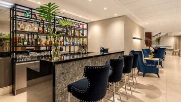 Eine Bar mit einer Marmorplatte, schwarzen Metallregalen und blauen, gepolsterten Barhocker.