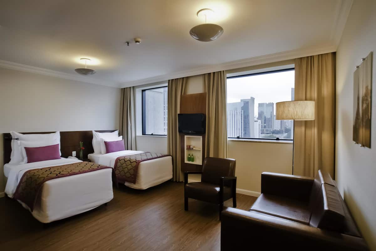 A hotel room with two beds, a chair, a TV, and a window with a city view.