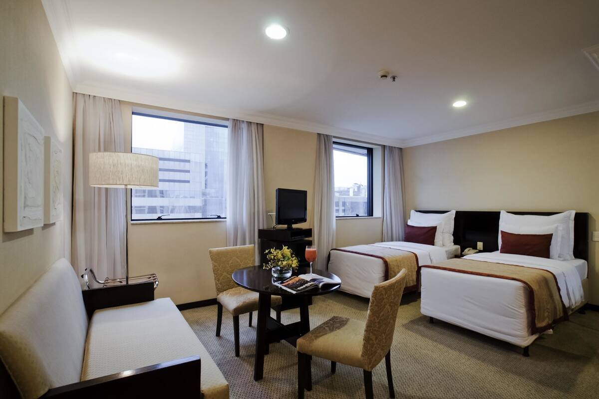 A hotel room with two beds, a desk, a chair, a TV, and a window with curtains.