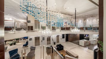 A spacious lobby with a modern chandelier, seating areas, and a glass railing overlooking the interior.