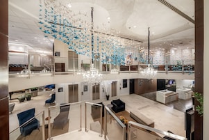 Um hall espaçoso com um lustre moderno, áreas de estar e guarda-corpo de vidro com vista para o interior.