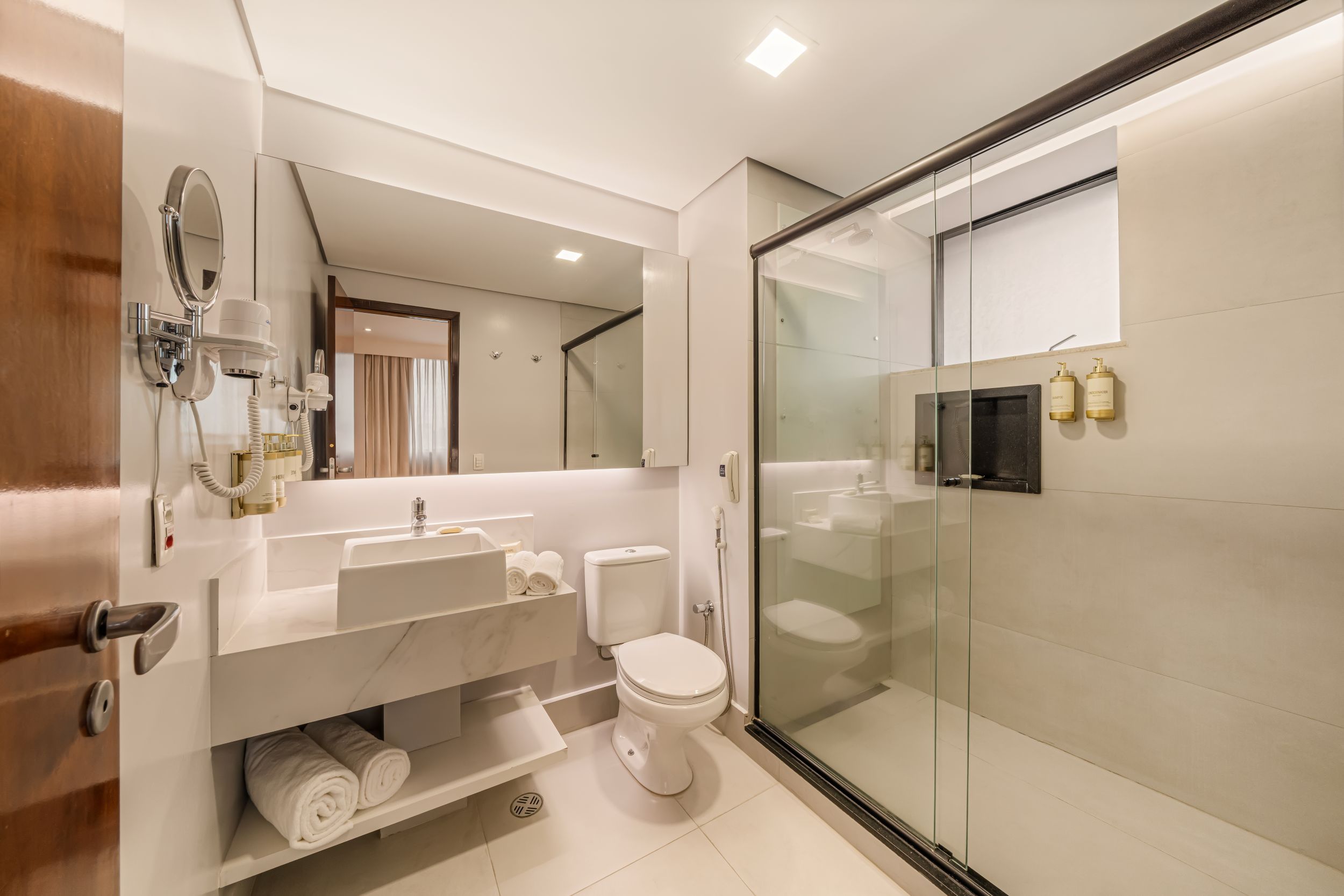 A modern bathroom with a glass shower enclosure, a white toilet, and a vanity with a mirror and towel rack.