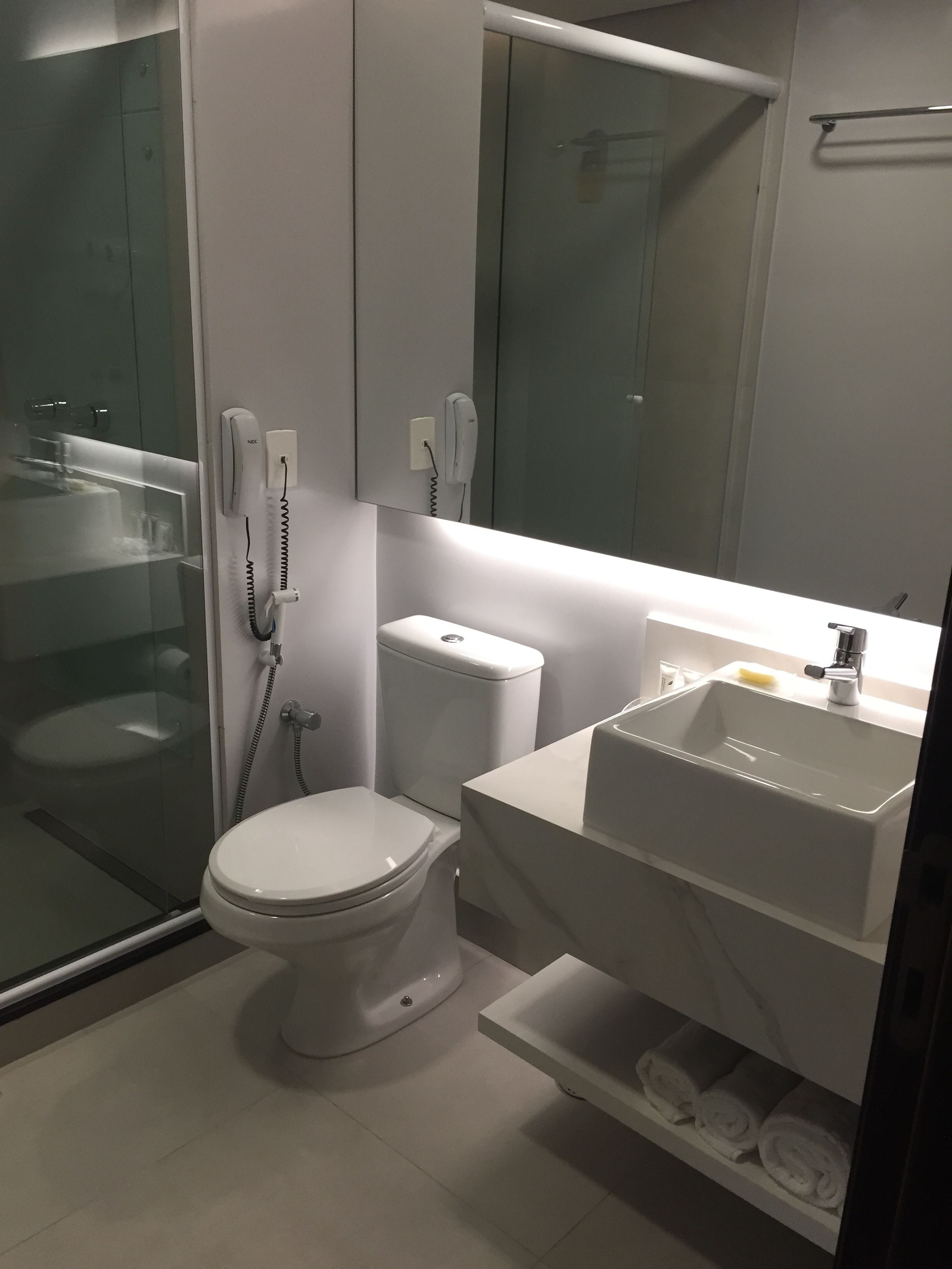 Een moderne badkamer met een glazen douchecabine, toilet, wastafel en spiegel.