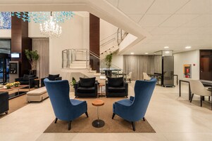 Um hall amplo com escadaria moderna, área de estar com poltronas e um balcão de recepção.
