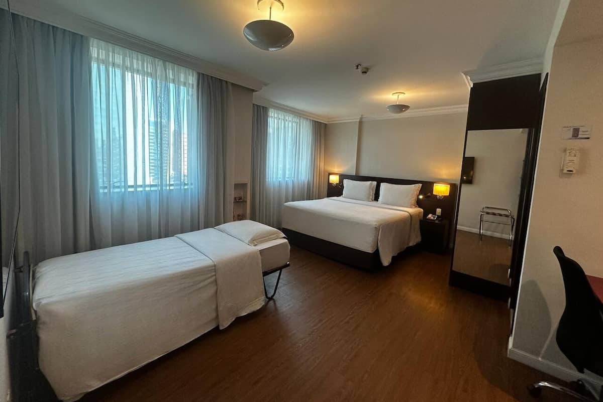 A hotel room with two single beds, a double bed, a bedside table with a lamp, a mirror, and a wooden floor.