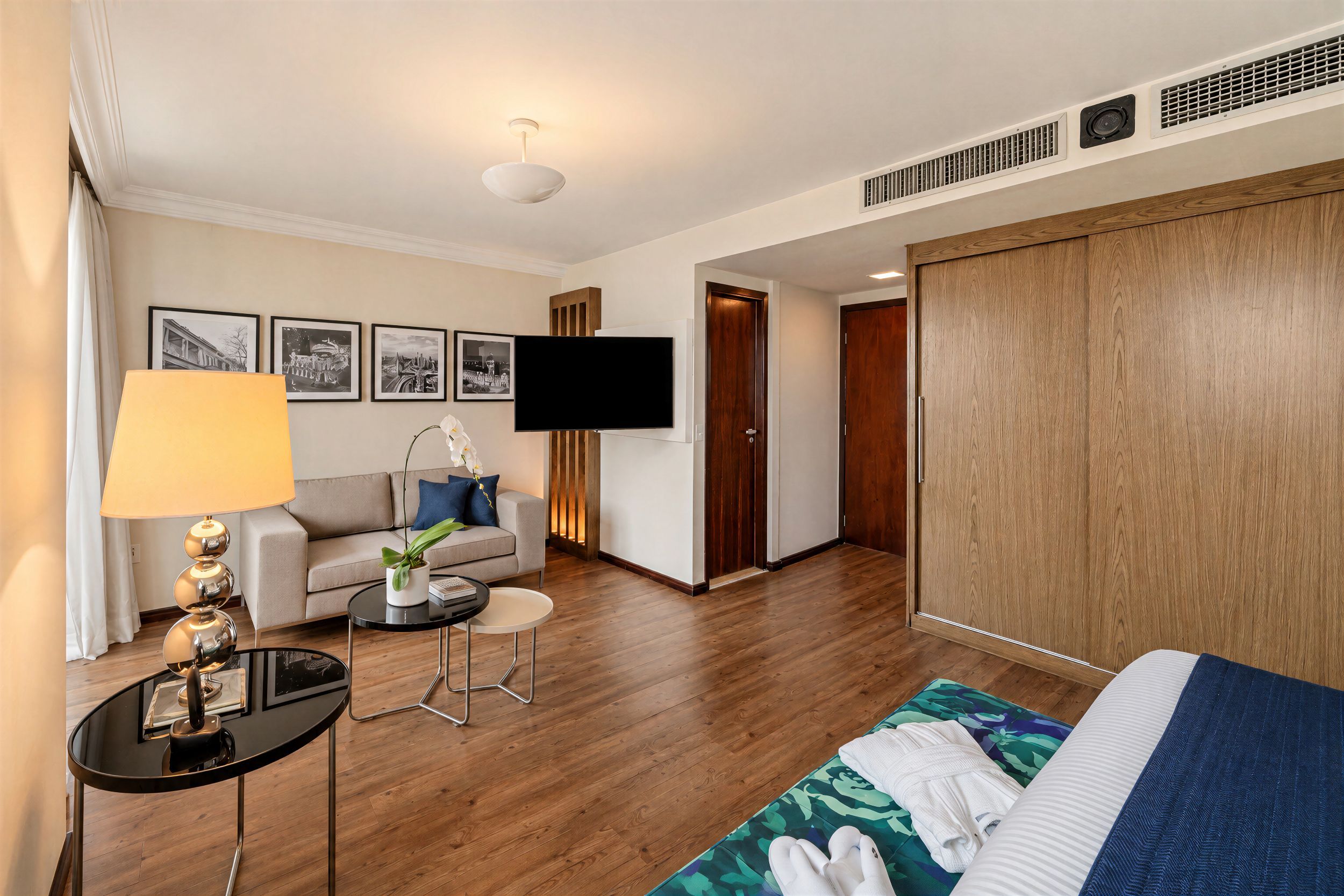 Habitación de hotel con cama, sofá, televisor, lámpara y una pequeña mesa.