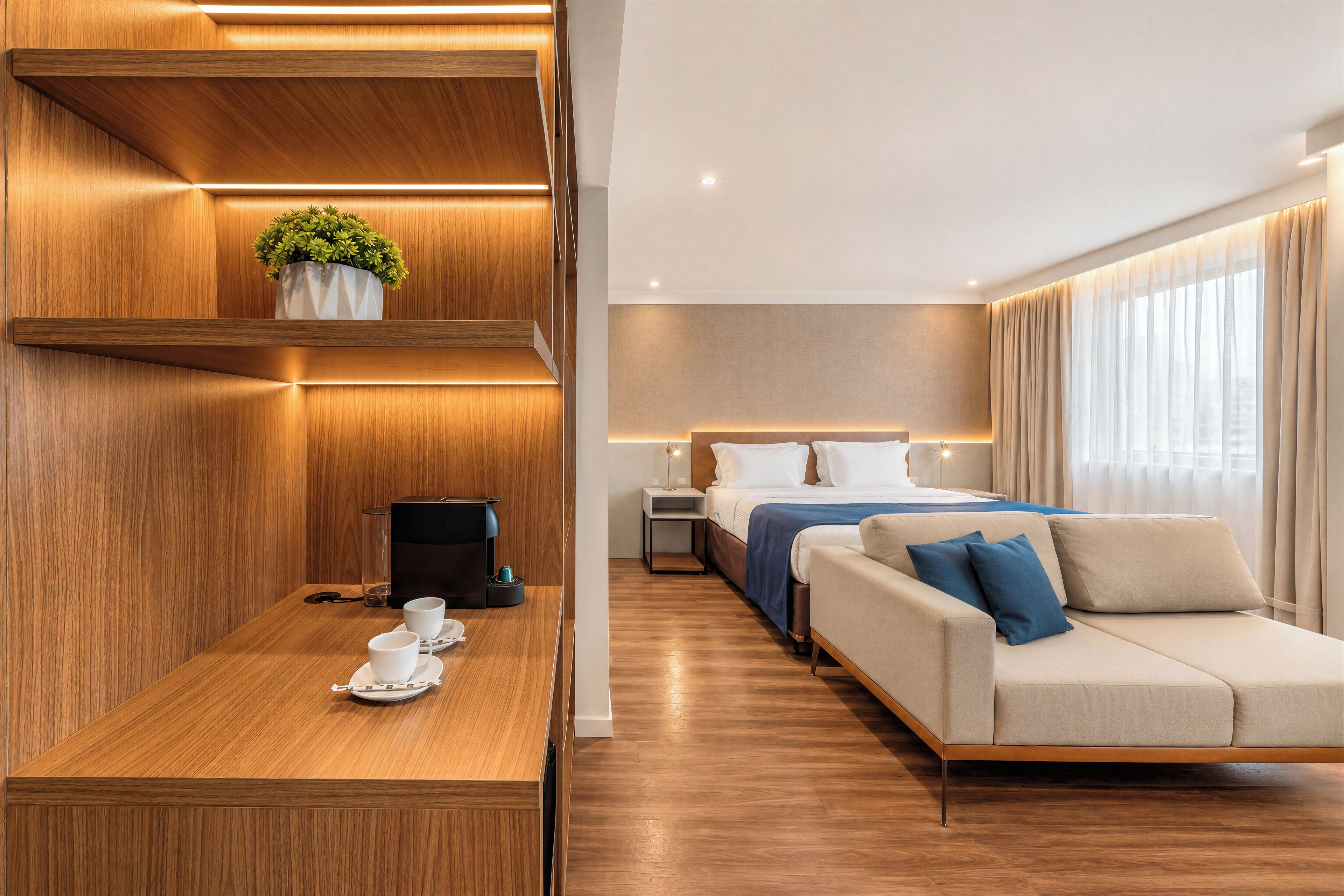 Une chambre d’hôtel avec un comptoir d’accueil en bois, un lit agrémenté d’un coussin bleu, un canapé et une table de chevet avec une lampe.