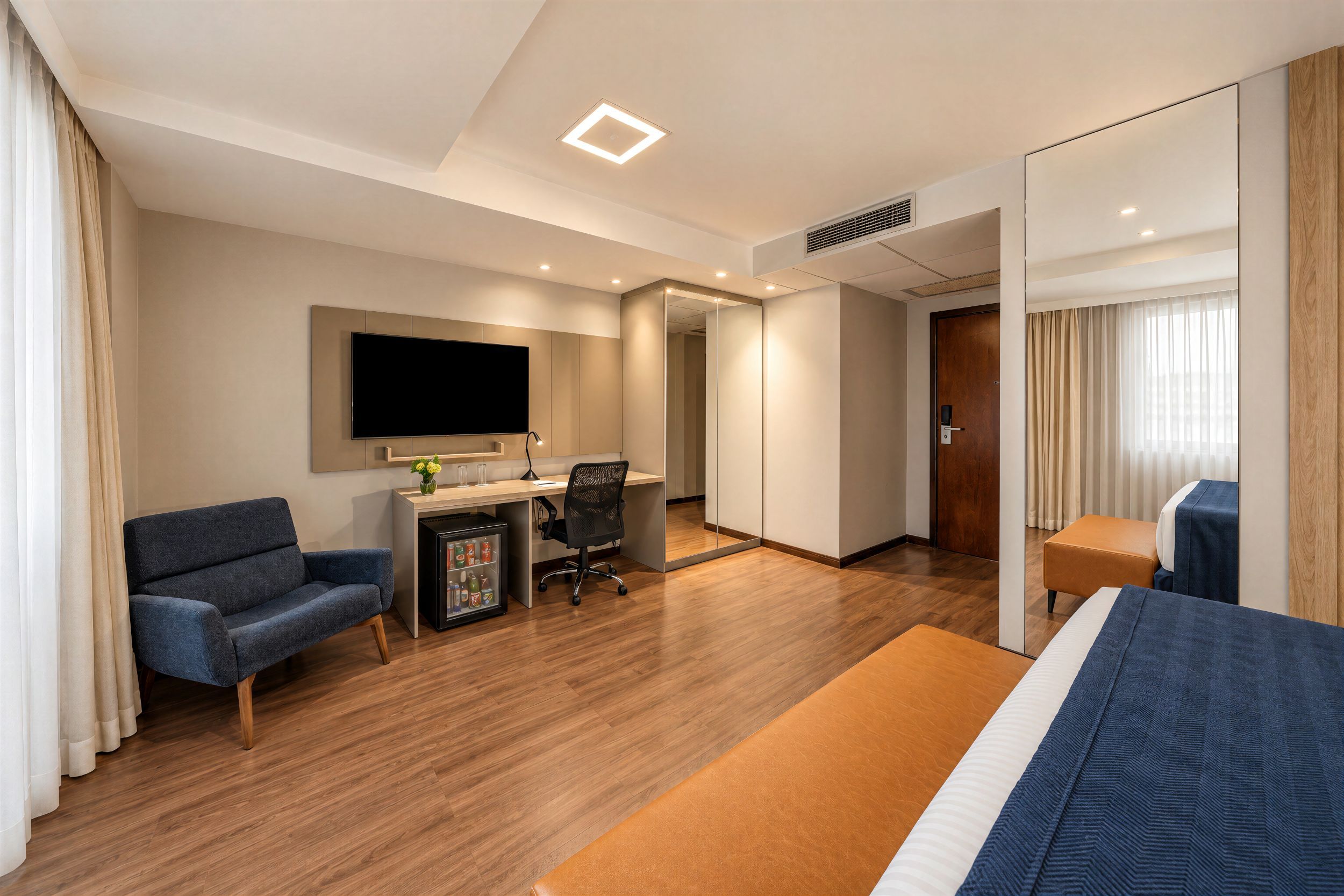 Ein Hotelzimmer mit Bett, Schreibtisch, Stuhl, Fernseher und einer Minibar.