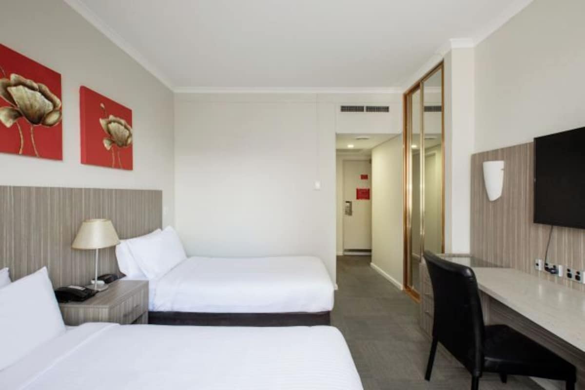 Camera d'albergo con due letti, una scrivania, una sedia, un televisore e opere d'arte alle pareti.