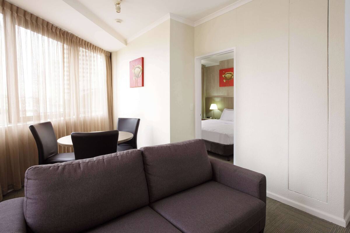 Ett hotellrum med en soffa, ett matbord med stolar, en säng och en spegel.
