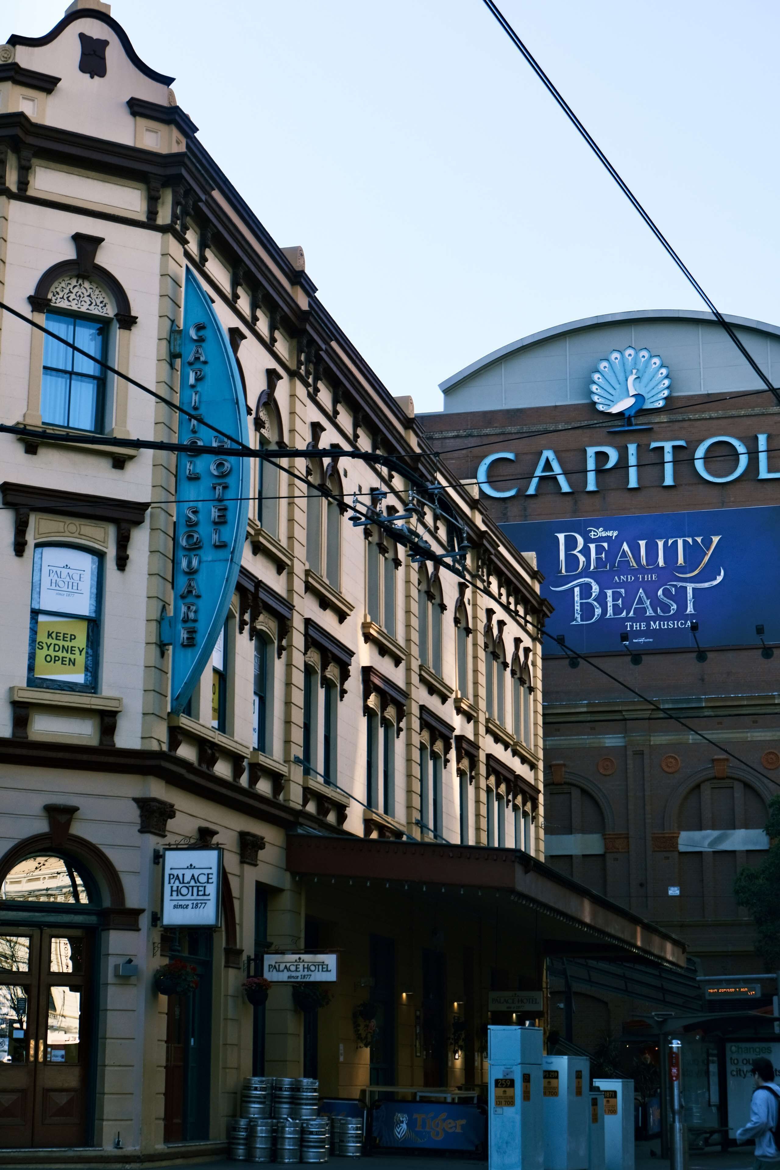 Un edificio histórico con un gran letrero azul del Capitol Hotel y un cartel anunciando la obra de Disney, La Bella y la Bestia.