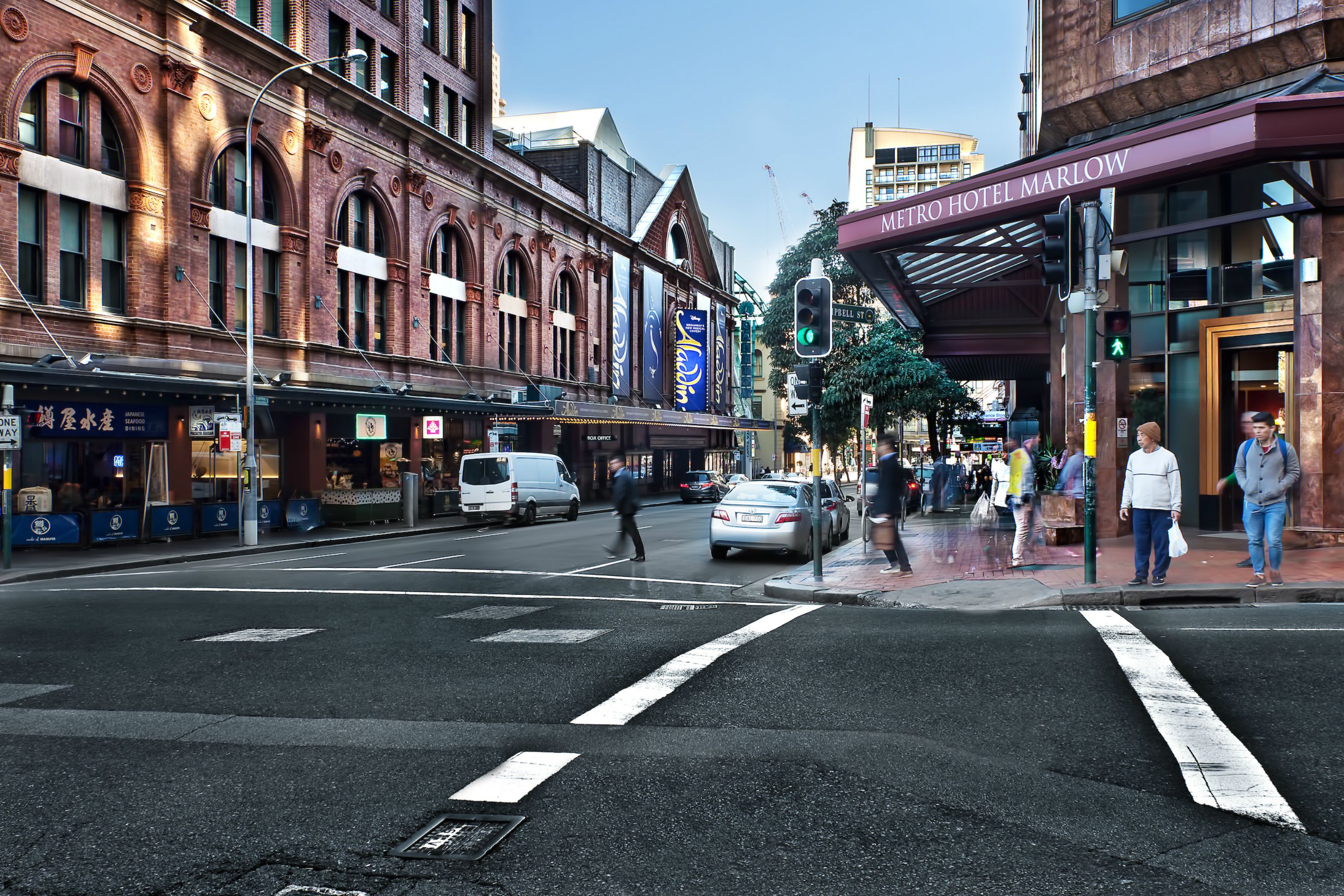 A street view with a Metro Hotel Marlow building, a pedestrian crossing, and a traffic light.