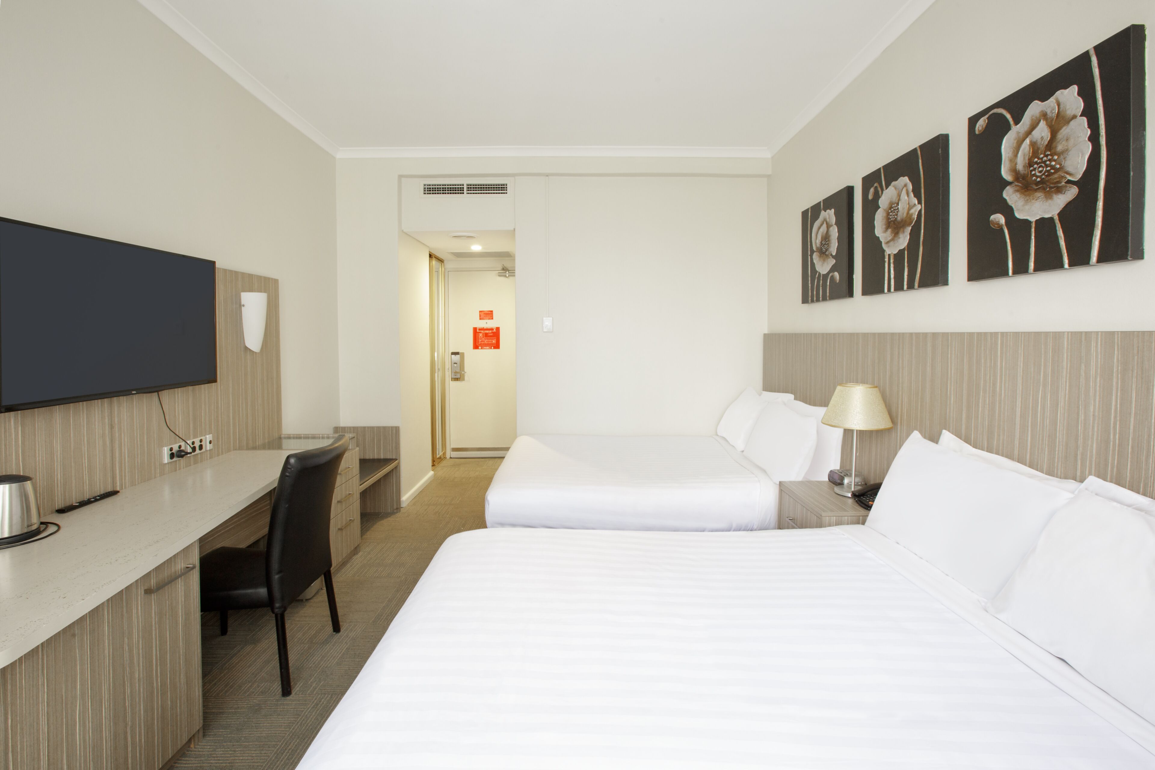 Une chambre d’hôtel équipée d’un lit, d’un bureau, d’une chaise, d’une télévision et d’œuvres d’art accrochées au mur.