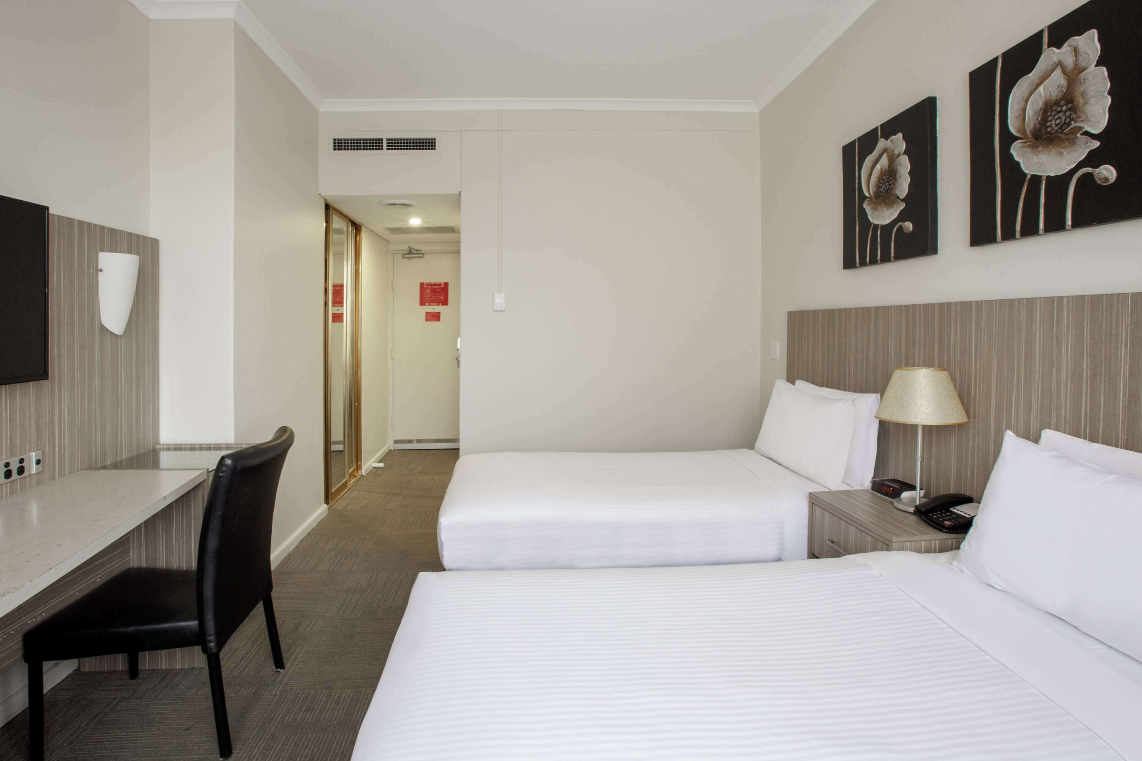 A hotel room with two beds, a desk, a chair, a lamp, and artwork on the wall.