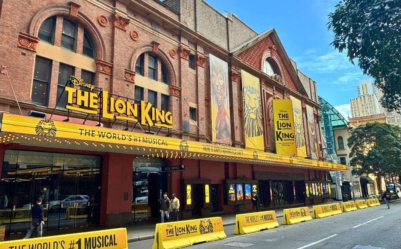 A theater building with 'The Lion King' signage, a brick facade, and a marquee.