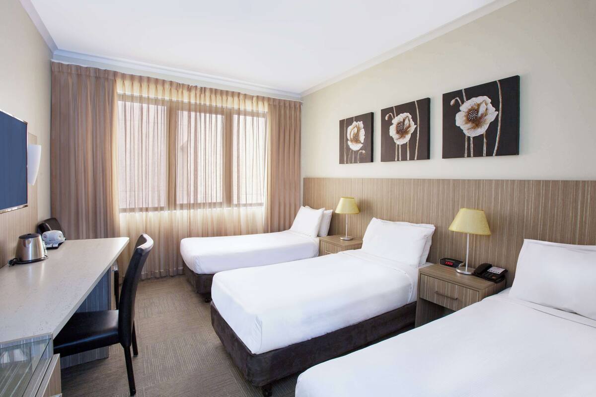 Ett hotellrum med två sängar, ett skrivbord, en stol, en TV och ett fönster med gardiner.