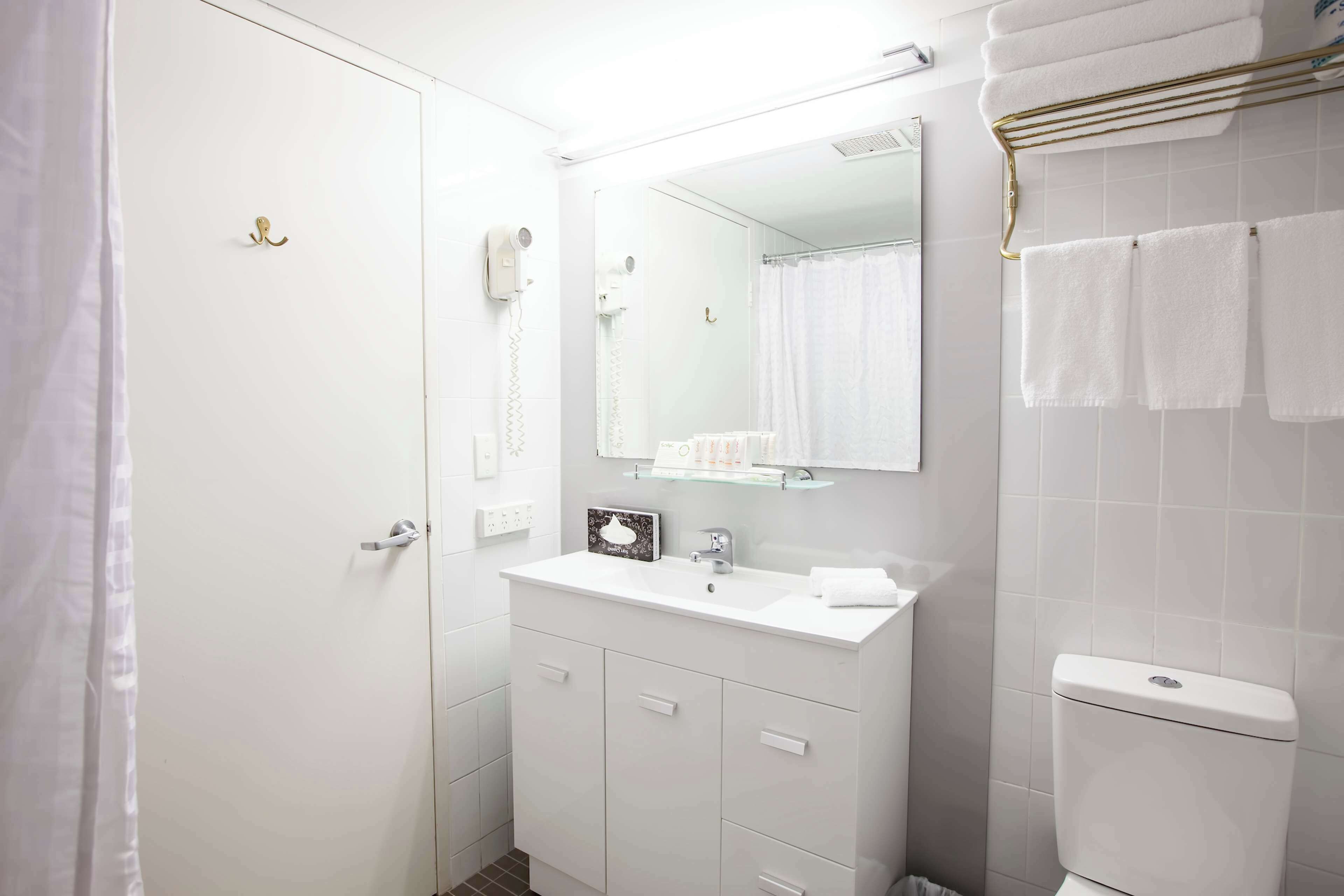 A modern bathroom with a white sink, vanity, and toilet. There is a glass shower enclosure and a towel rack above the toilet.