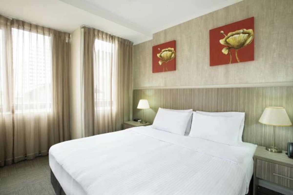 Una camera d'albergo con un letto grande, due lampade sui comodini e due dipinti di fiori appesi al muro.