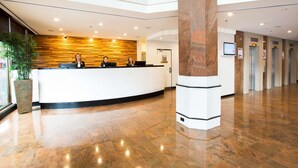 A reception area with a curved reception desk, a large pillar, and a plant to the left. - Metro Hotel Marlow Sydney Central (Haymarket)