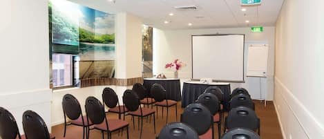 A conference room with rows of chairs, a projector screen, and a whiteboard.