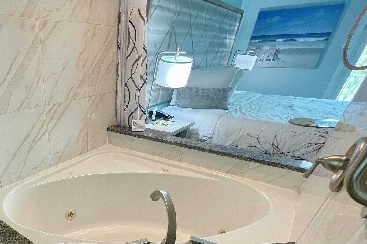 Uma casa de banho moderna com uma banheira grande, toucador com espelho e cama com vista para o oceano.