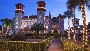 Un edificio histórico con dos torres, ventanas arqueadas y un jardín bien iluminado con palmeras.